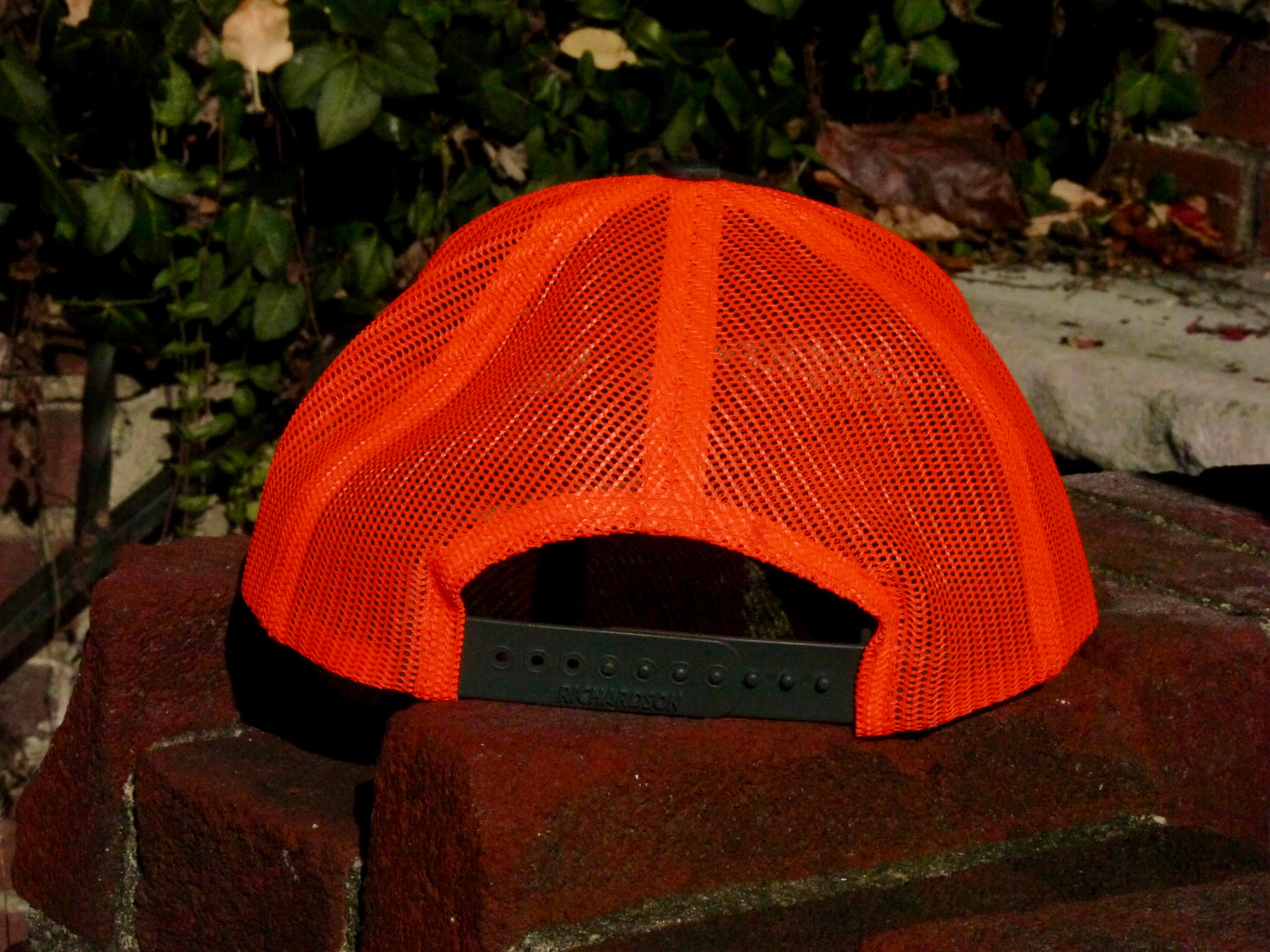 Rear view of the orange mesh back of the hat and the charcoal snap to size the hat.